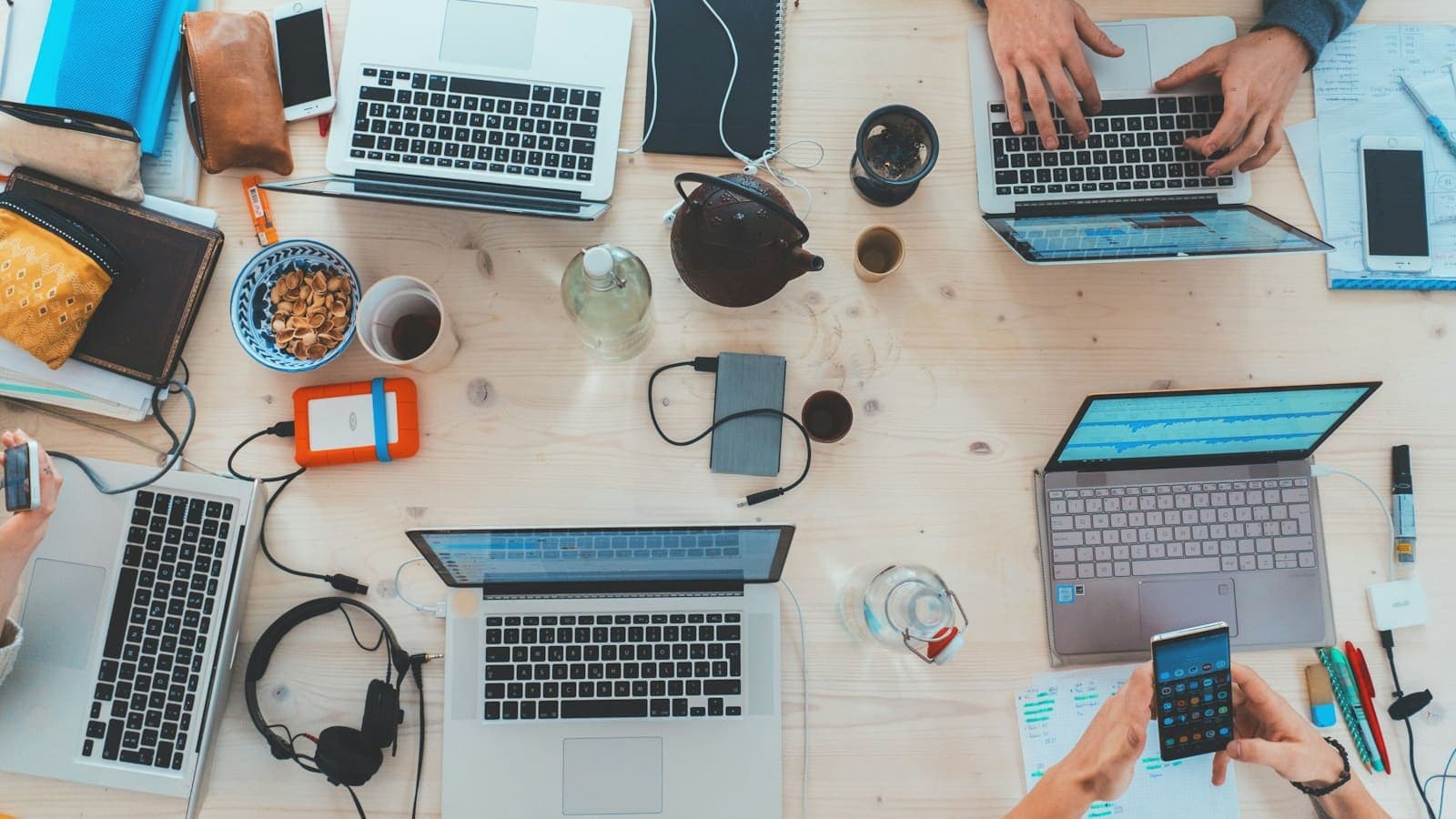 Laptops, notebooks and a phone on a shared wooden desk, seen from above